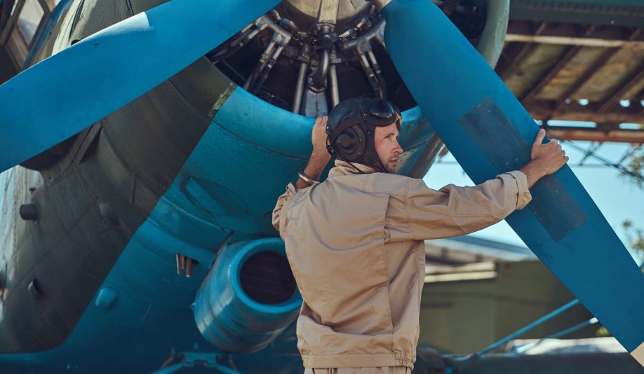 Pilot or mechanic in a full flight gear checks the propeller of his retro military aircraft before the flight.