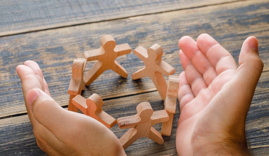 business-success-concept-on-wooden-table-top-view-hands-protecting-wooden-figures-of-people (1) (1)